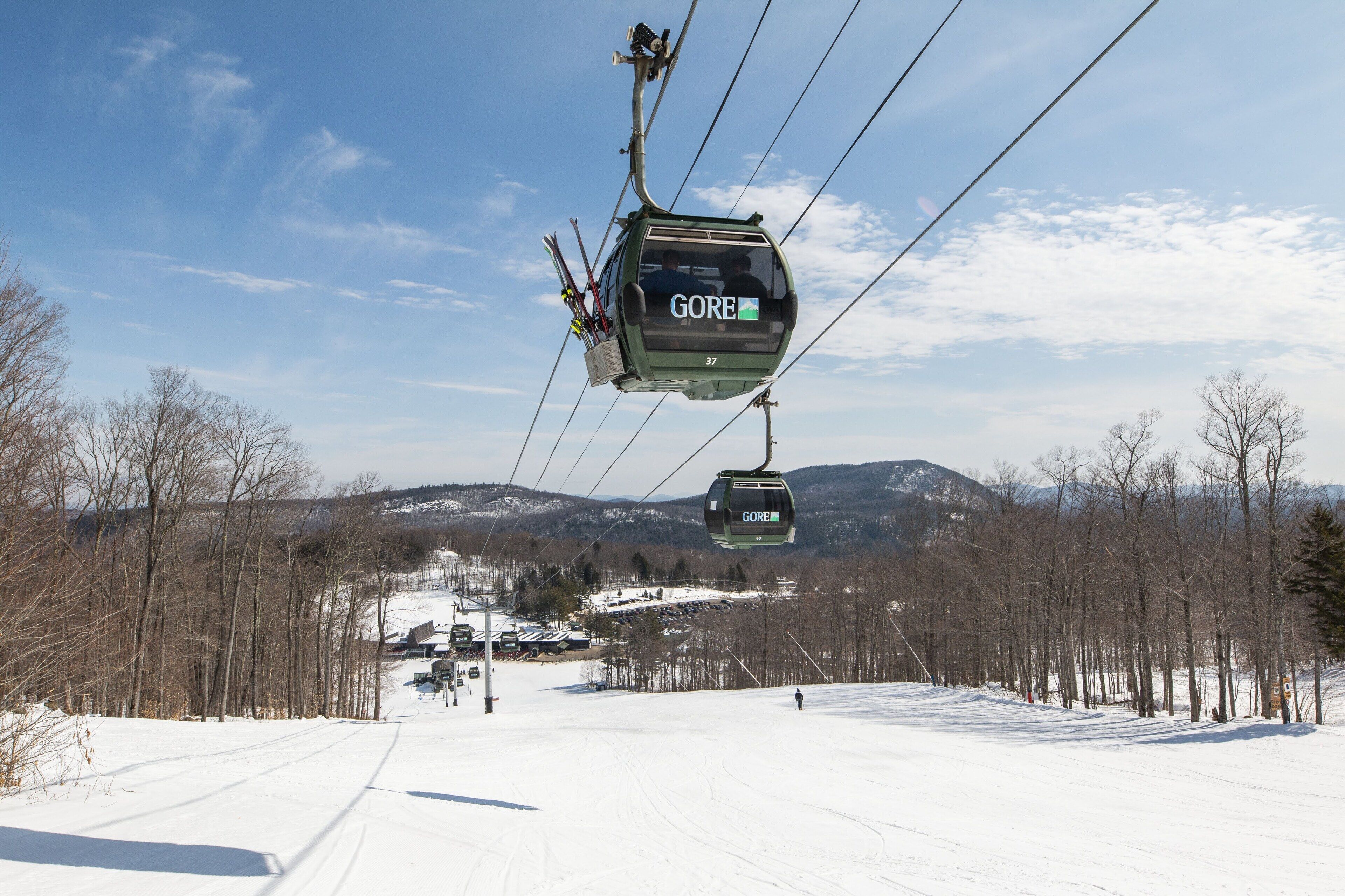 Un teleférico con la etiqueta "GORE" asciende por una pendiente nevada, con cielo despejado y montañas al fondo.