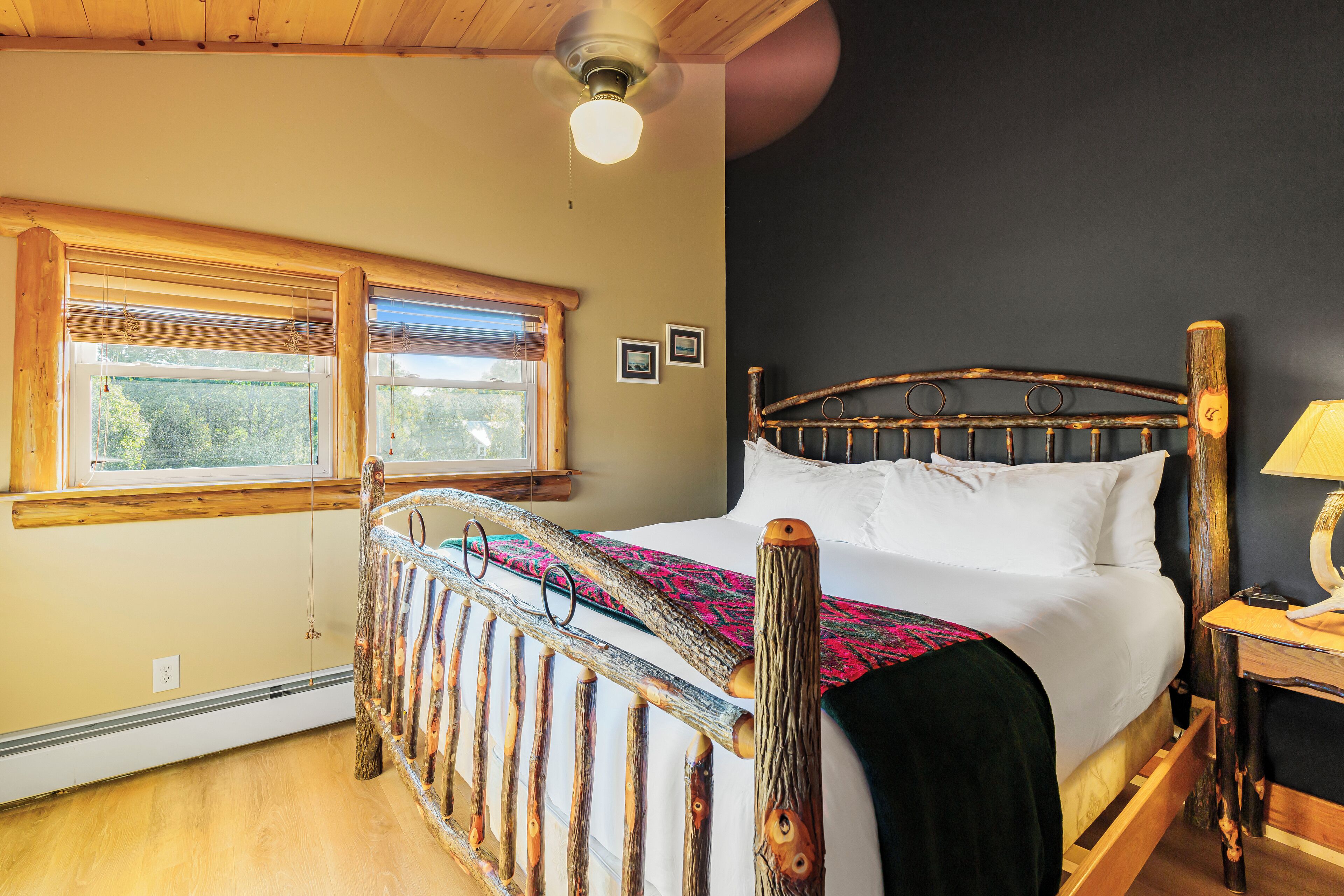 A wooden bed with a headboard, a window with blinds, and a ceiling fan.