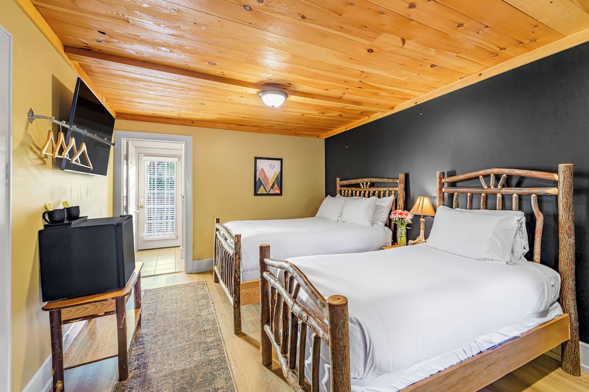 A room with two wooden beds, a television on a small table, and a door with blinds.