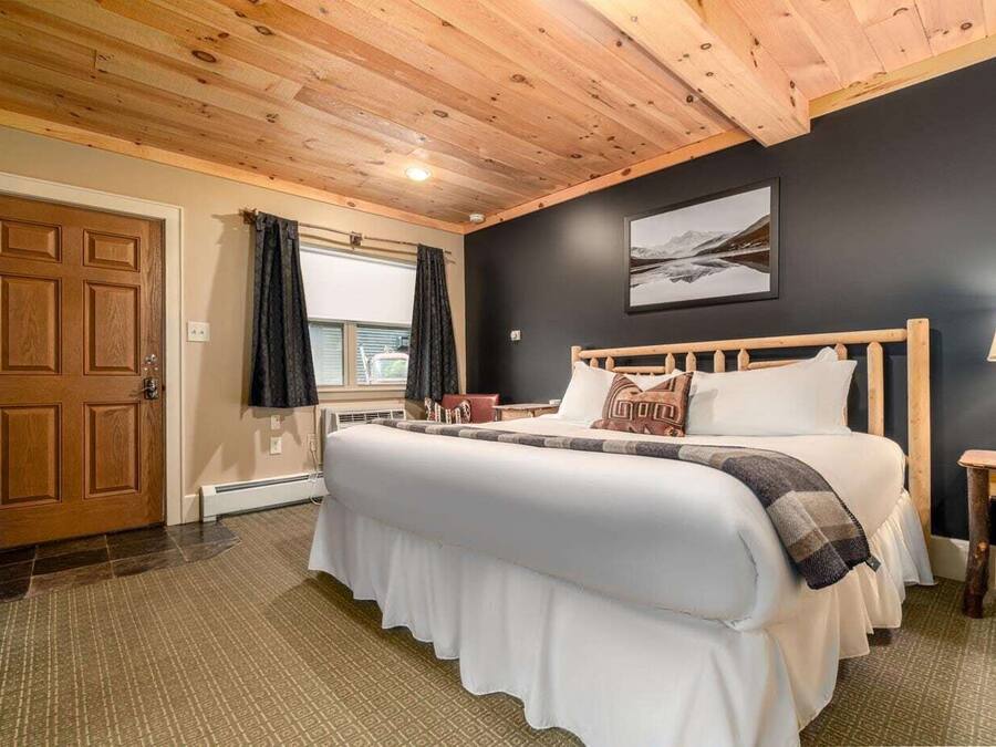 A bedroom with a large bed, wooden headboard, a nightstand, a lamp, and a window with curtains.