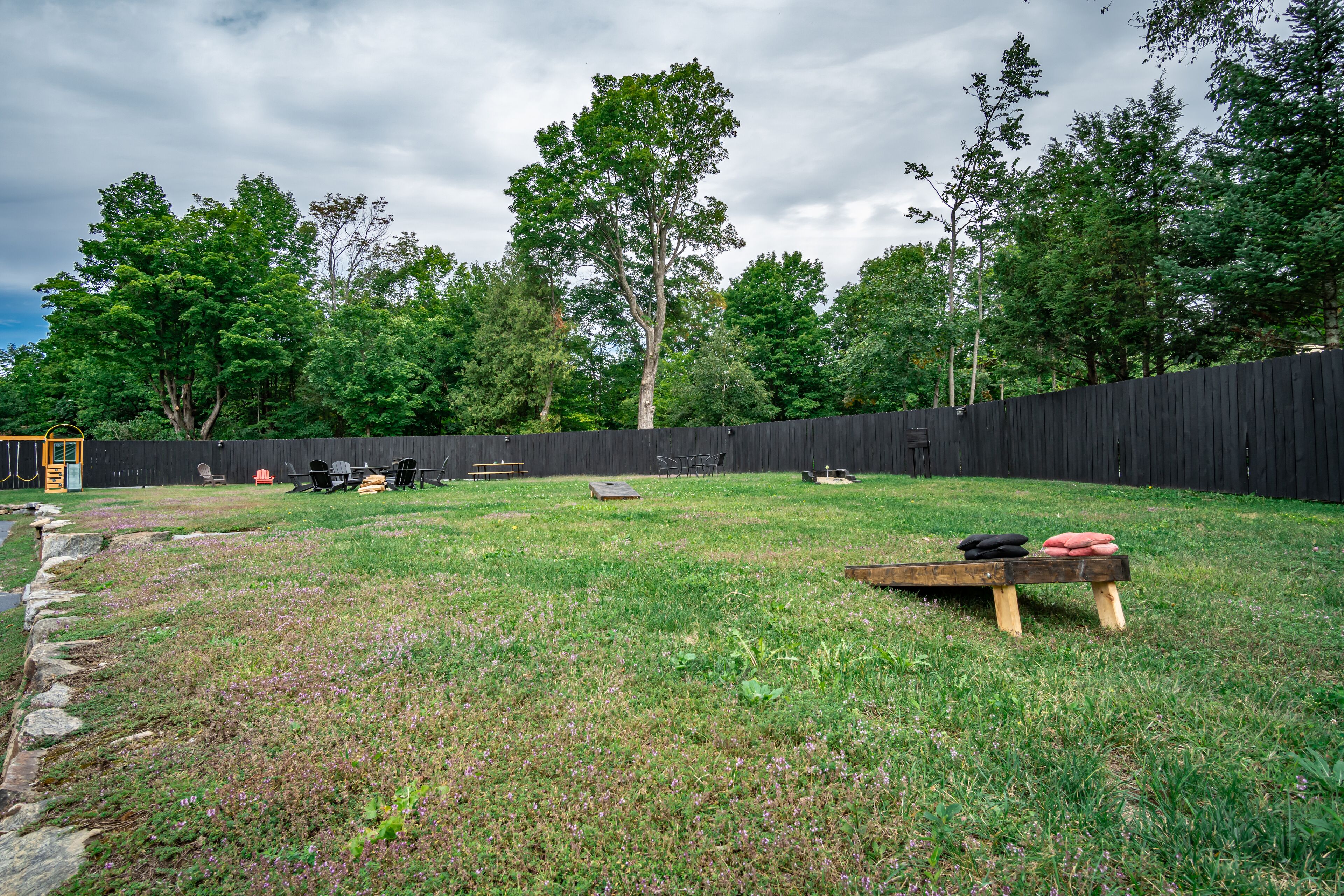 A grassy backyard with a wooden bench, picnic table, and outdoor furniture.