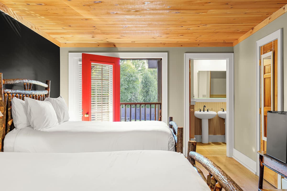 A bedroom with two beds, a wooden ceiling, a red door, and a view of the outdoors.