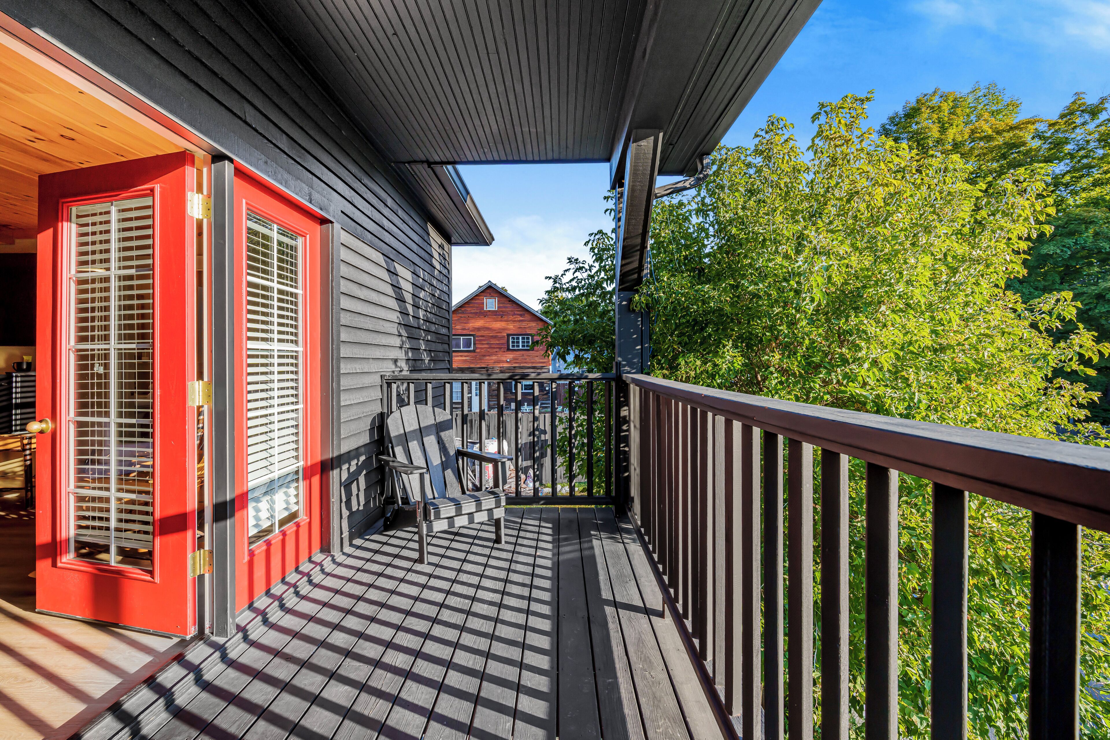 A wooden deck with a red door and a view of a house in the background.