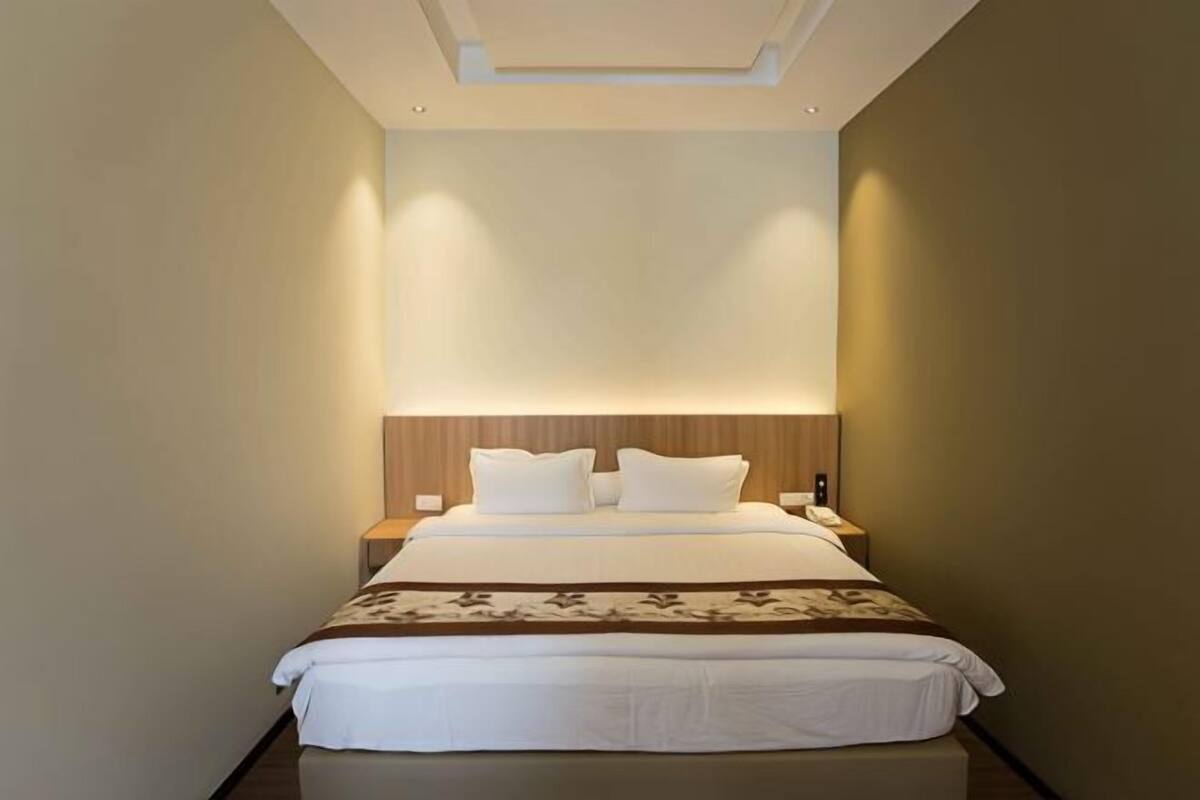 Ein modernes Hotelzimmer mit einem großen Bett, einem Holzkopfende und einem Nachttisch mit Lampe.