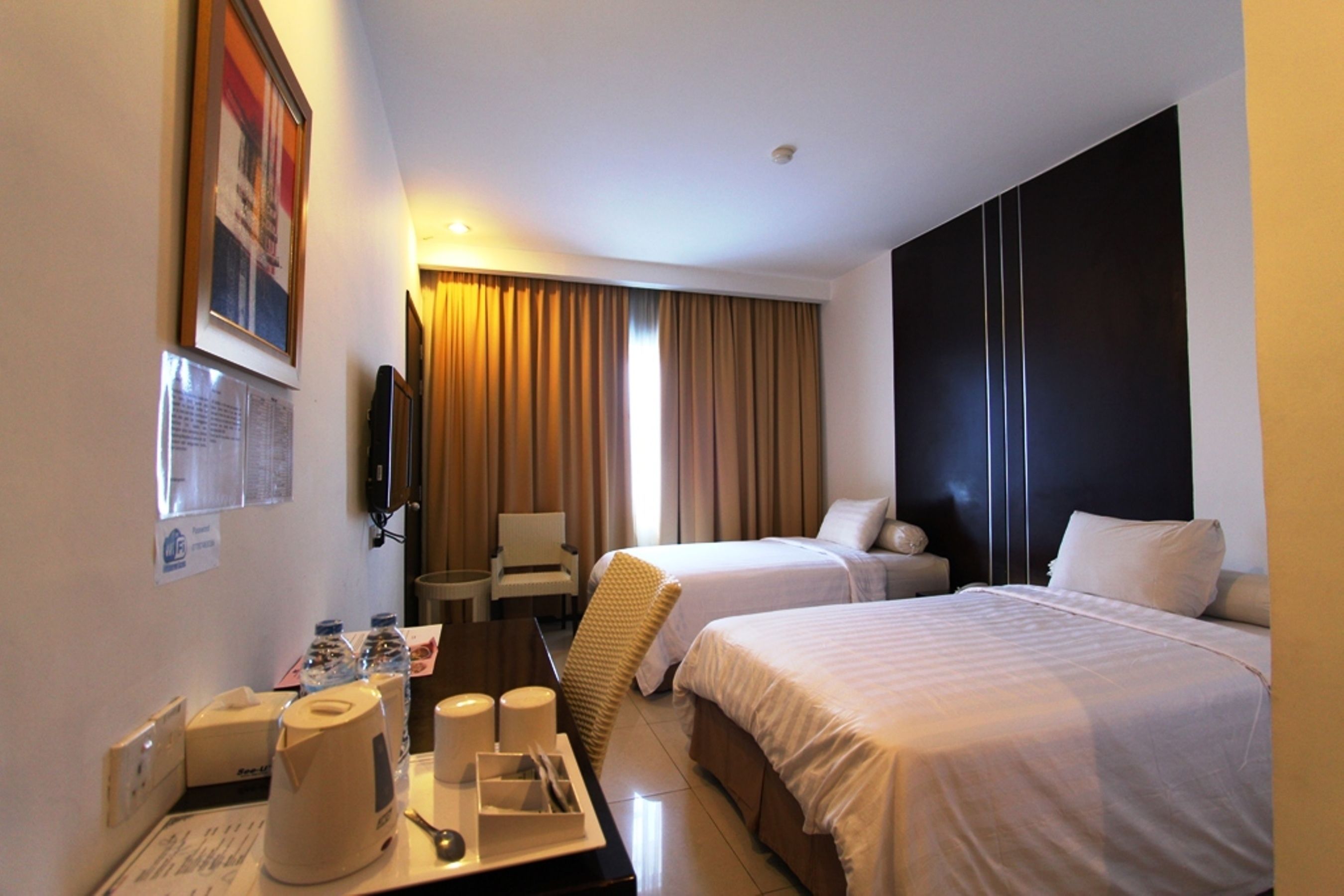 Habitación de hotel con dos camas, un escritorio con teléfono, una silla y un televisor en la pared.