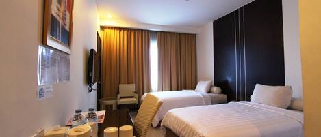 Habitación de hotel con dos camas, un escritorio con teléfono, una silla y un televisor en la pared.