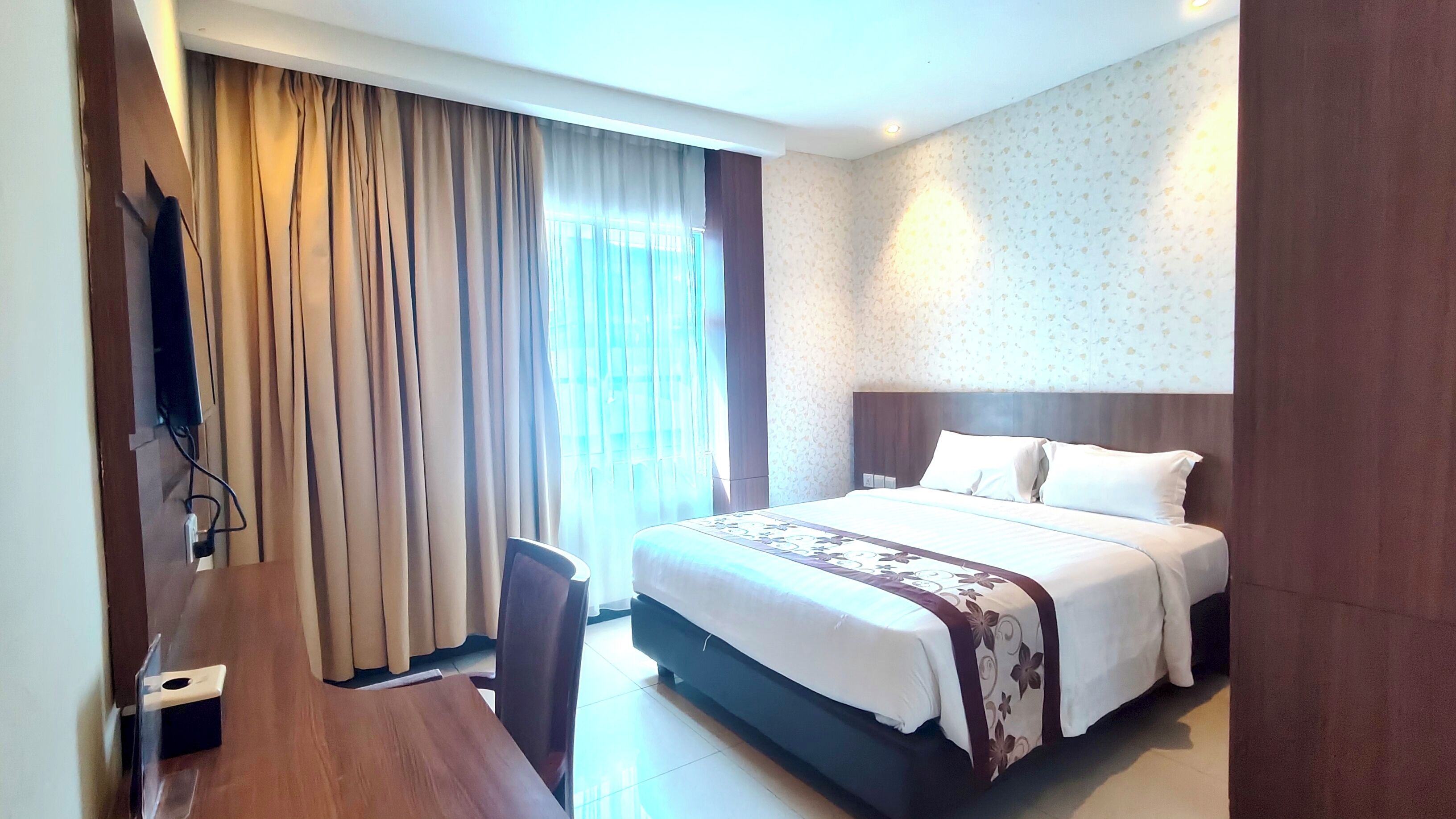 Quarto de hotel com cama, escrivaninha, cadeira e televisão.