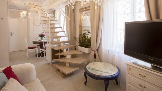 A spacious living area with a staircase, a dining table with chairs, a sofa, a television, and a decorative plant. - Antique Apartments Old Town (Kraków)