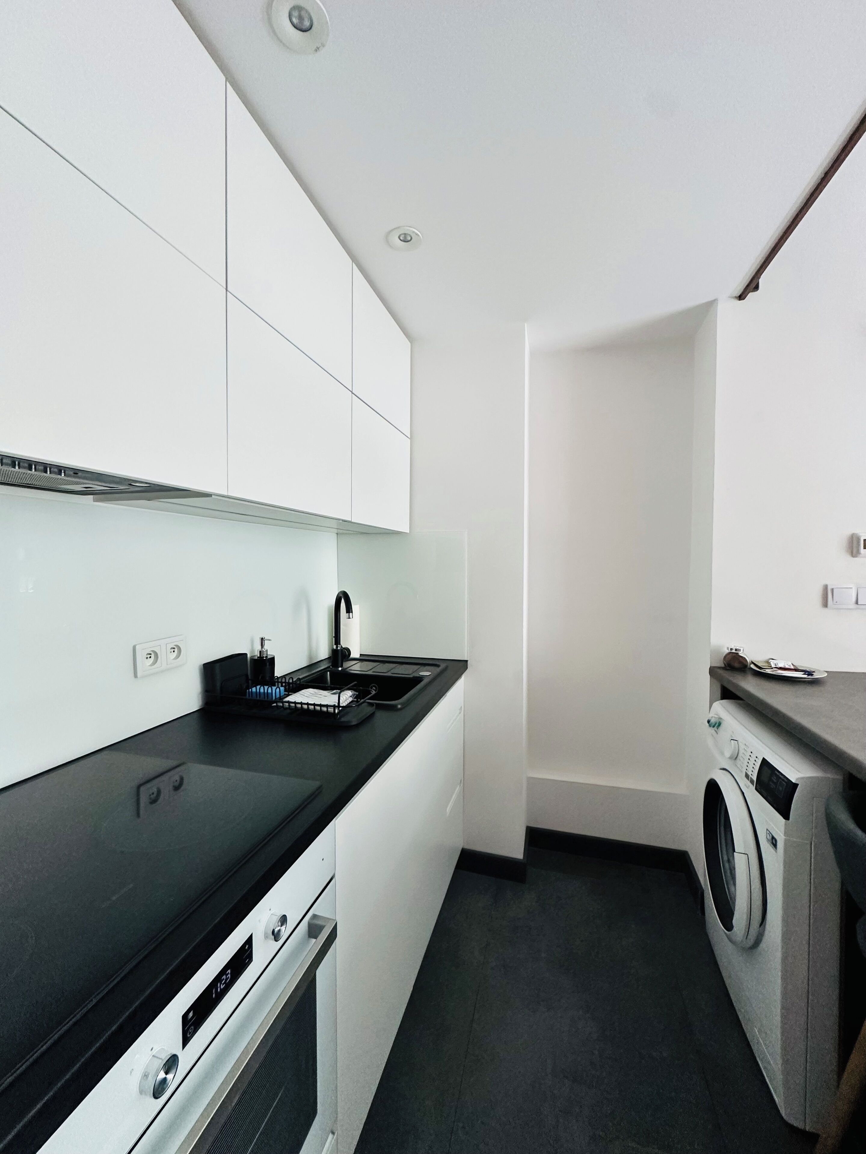 A compact kitchen with a black countertop, white cabinets, a built-in washing machine, and a small sink.