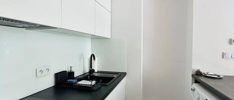 A compact kitchen with a black countertop, white cabinets, a built-in washing machine, and a small sink.