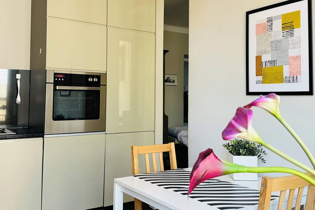 Een moderne keuken met witte kasten, een ingebouwde oven en een eethoek met een witte tafel en houten stoelen.