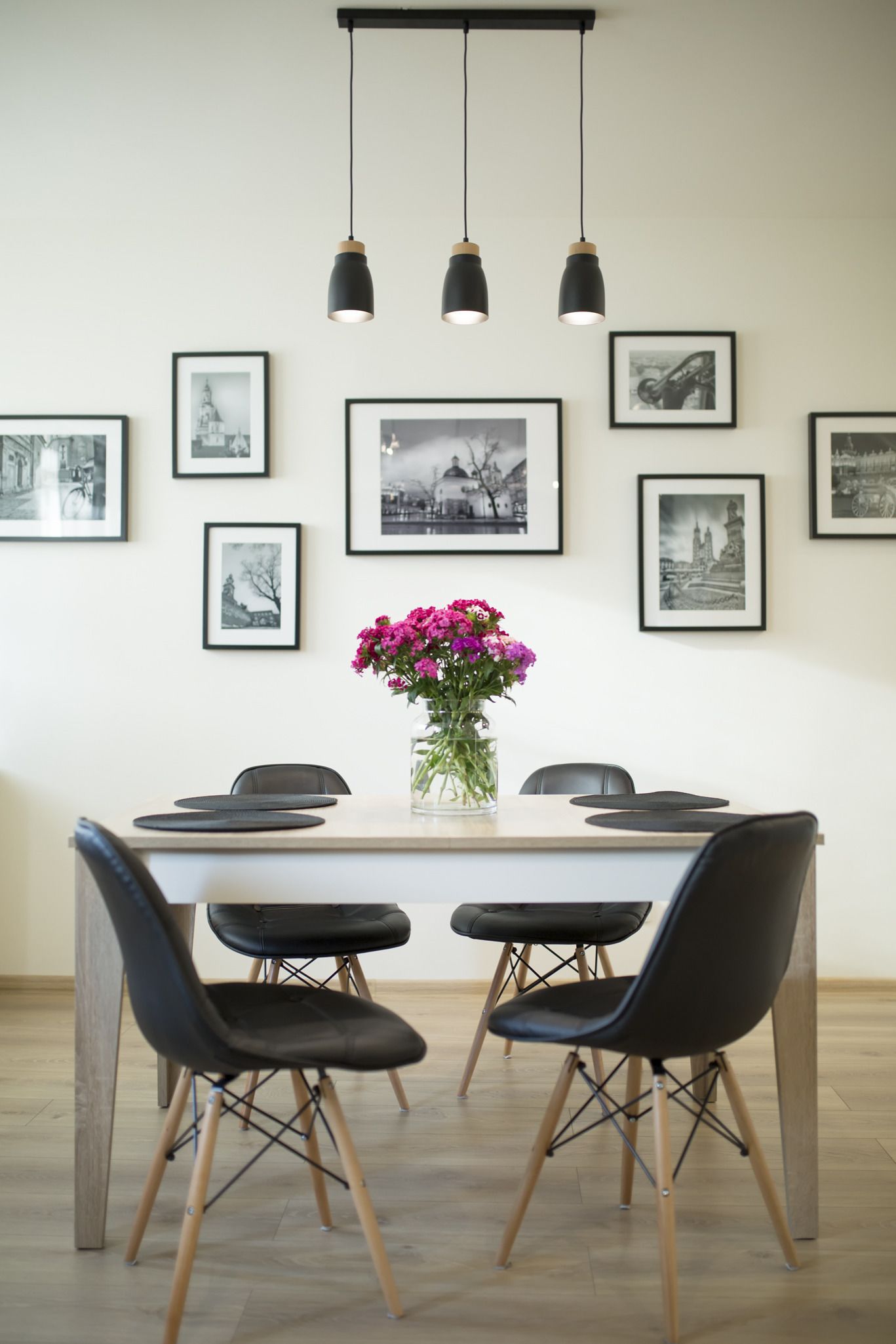 A dining area with a white table, black chairs, and a vase of pink flowers.