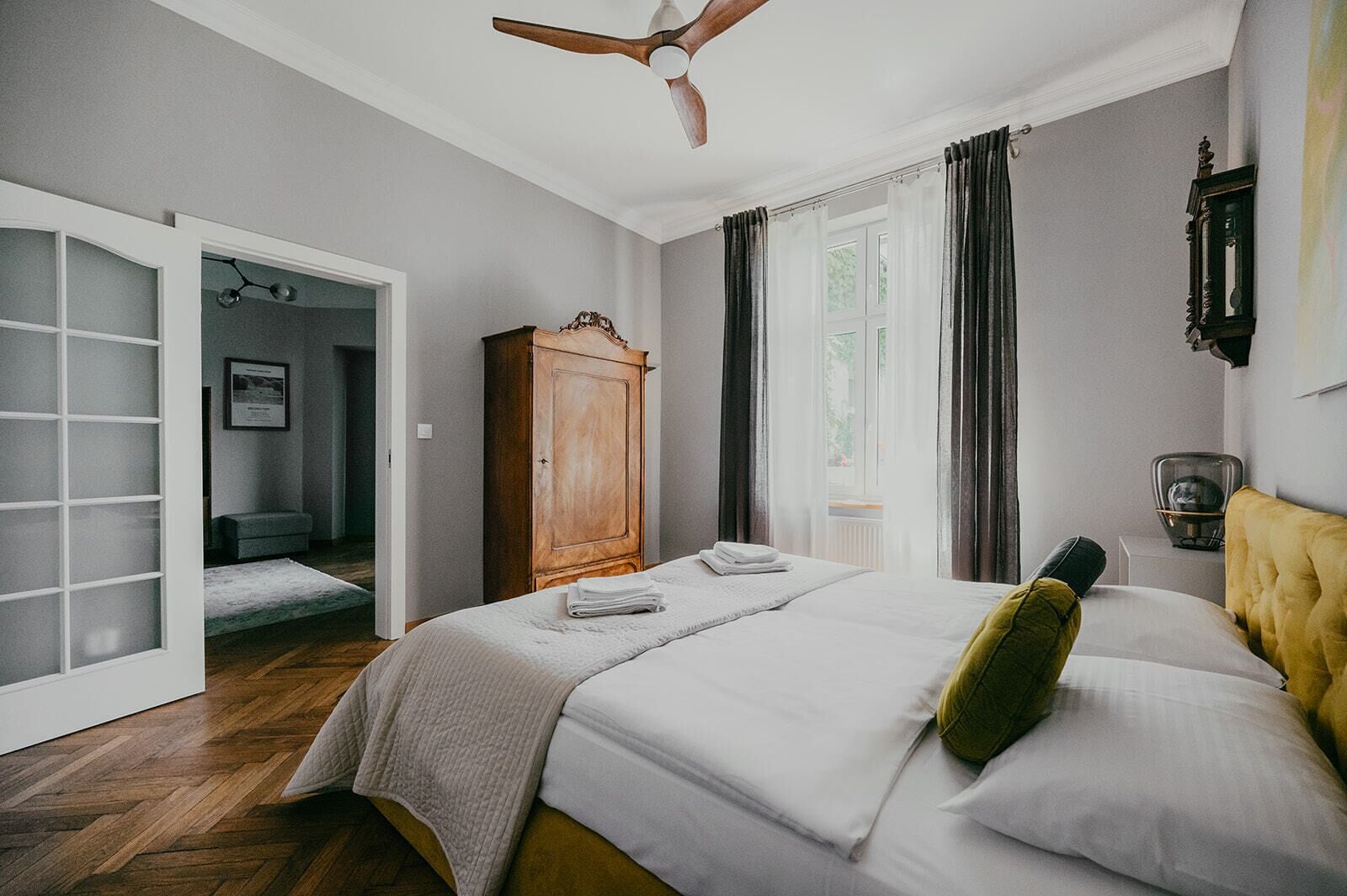 A bedroom with a bed, a wardrobe, a ceiling fan, and a window with curtains.