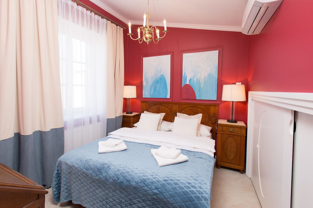 Een hotelkamer met een bed, twee nachtkastjes, een kroonluchter en kunst aan de muur.