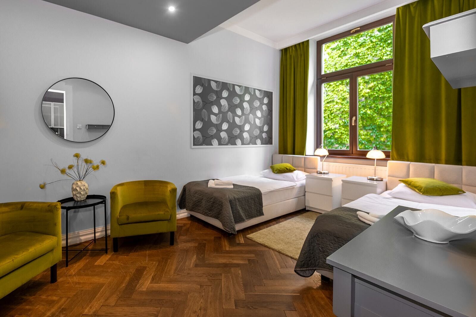 Een moderne slaapkamer met twee bedden, een ronde spiegel en een groene fauteuil.