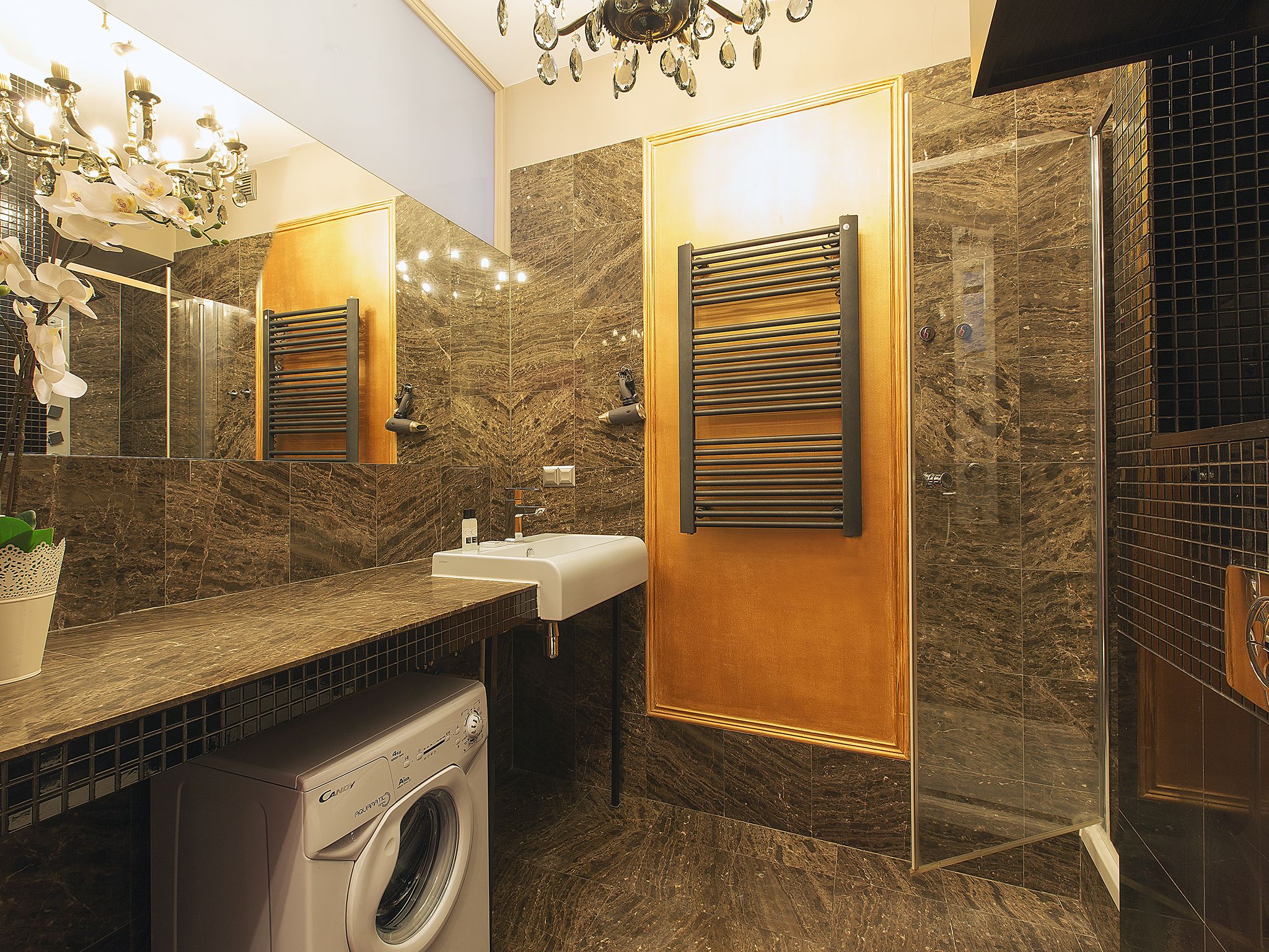 A modern bathroom with a marble wall, a sink, a mirror, a towel rack, and a washing machine.