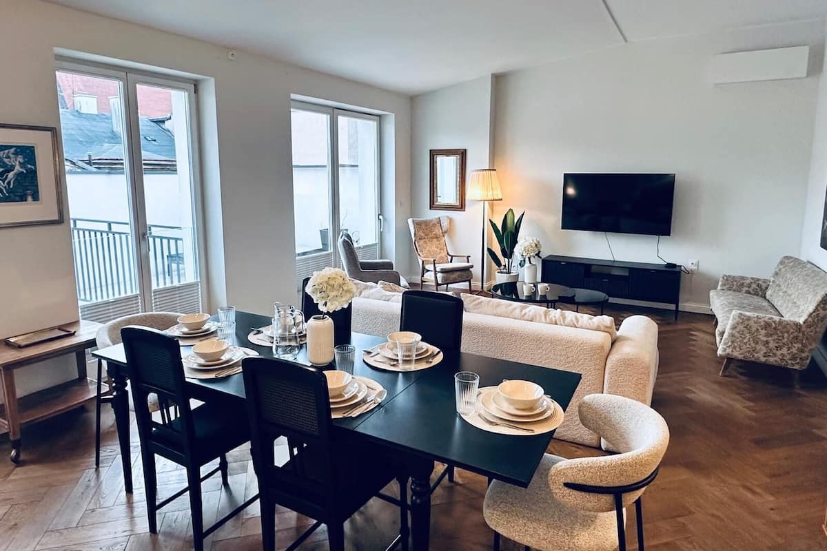 Een moderne woonkamer met een eethoek, een zithoek, een televisie en een balkon met grote ramen.