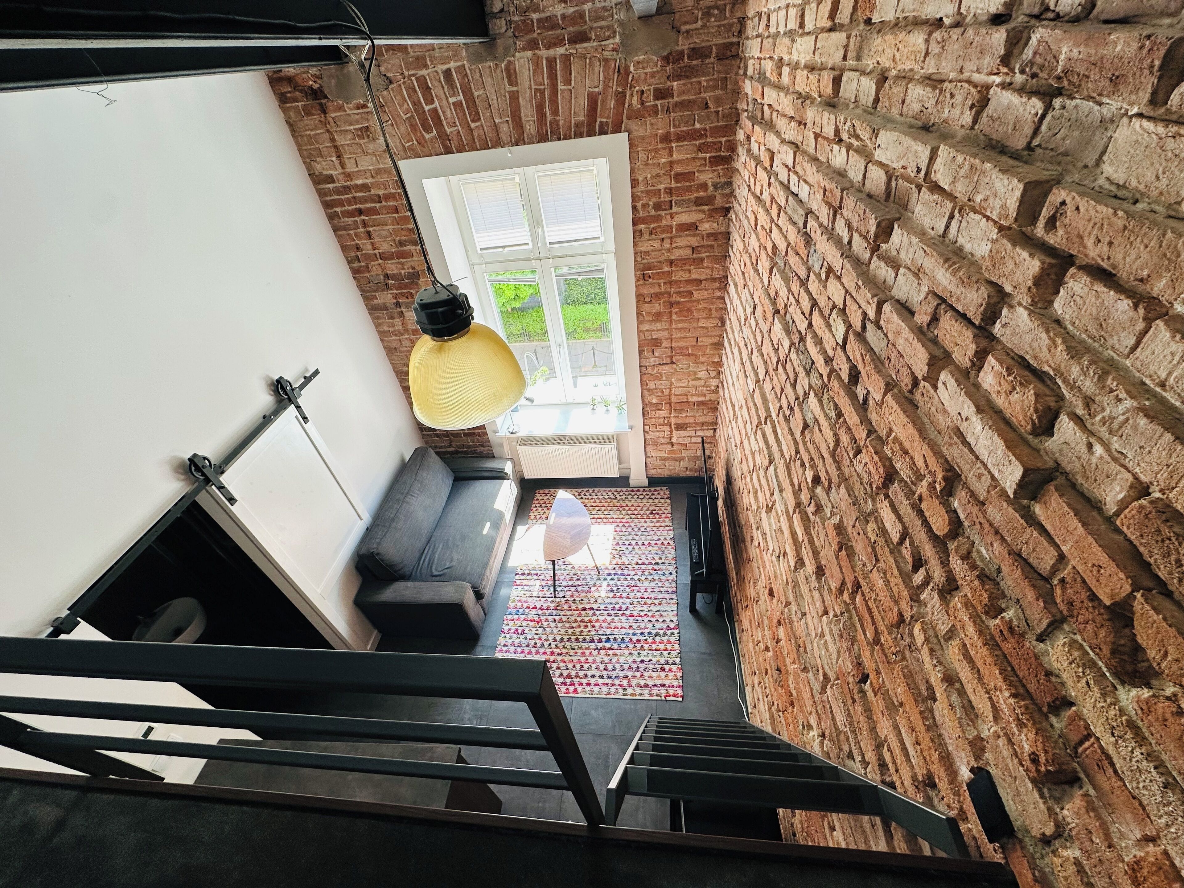 Un escalier menant à une pièce avec un mur en briques, une fenêtre et un canapé.
