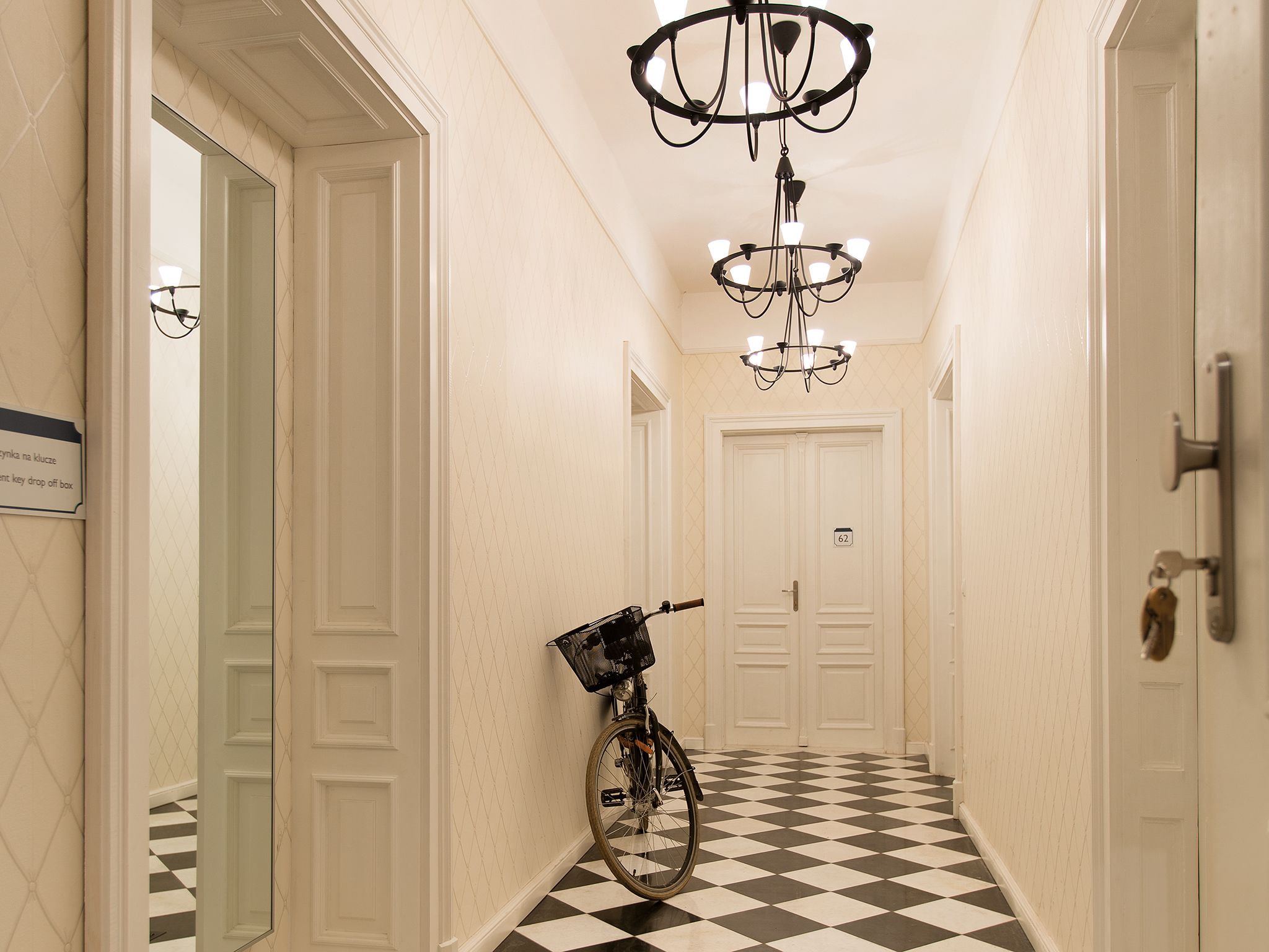 Um corredor com piso xadrez, uma bicicleta e um candelabro.