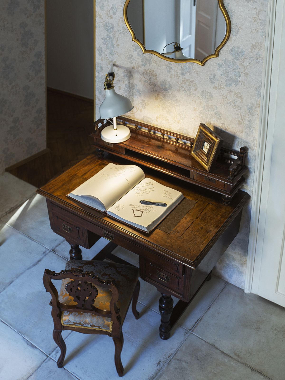 A wooden desk with an open book, a lamp, and a mirror.