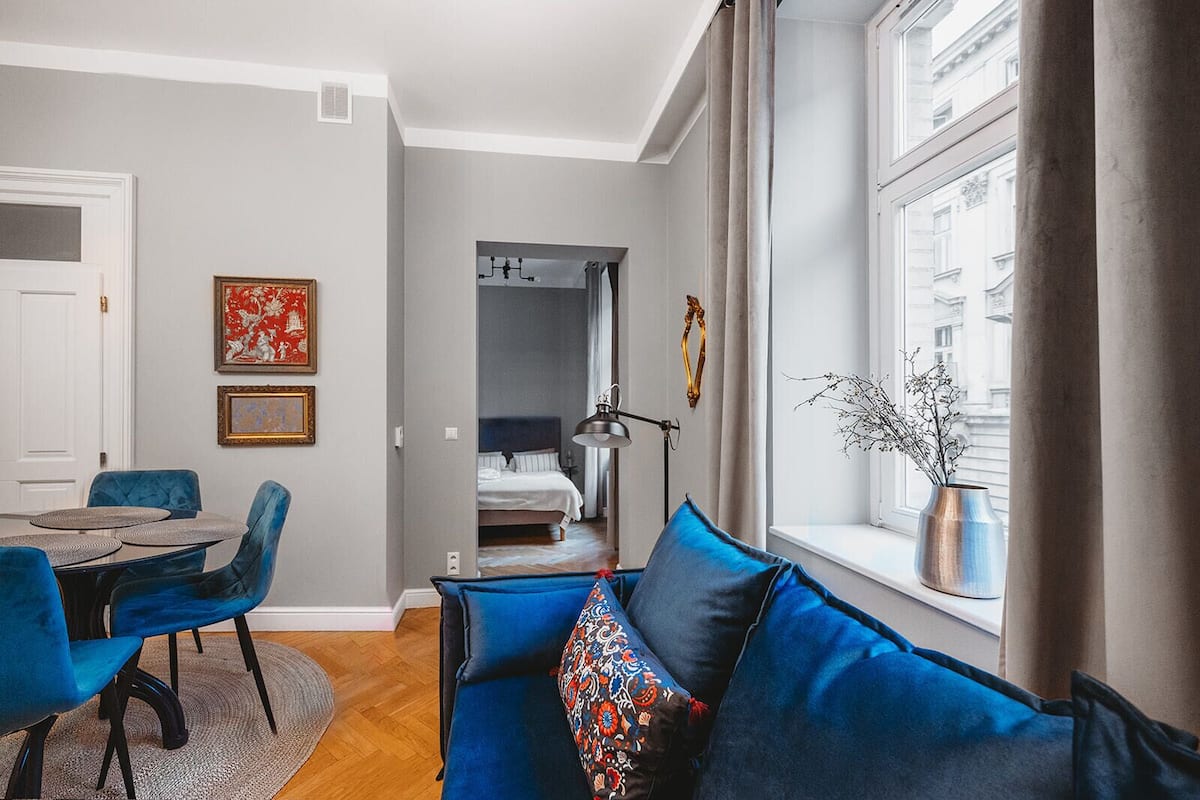 Een moderne kamer met een blauwe bank, een eettafel met stoelen, en een bed op de achtergrond.