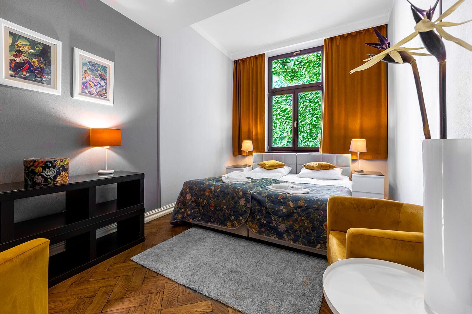 A hotel room with a bed, bedside tables, a desk, a chair, and artwork on the wall.