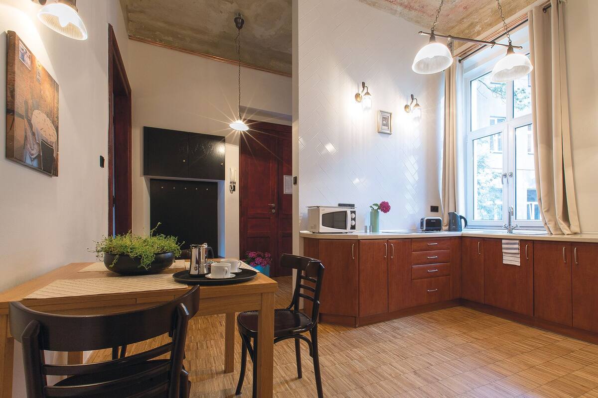 Een keuken met houten kasten, een eettafel met stoelen, een koffiezetapparaat, een magnetron en een broodrooster.