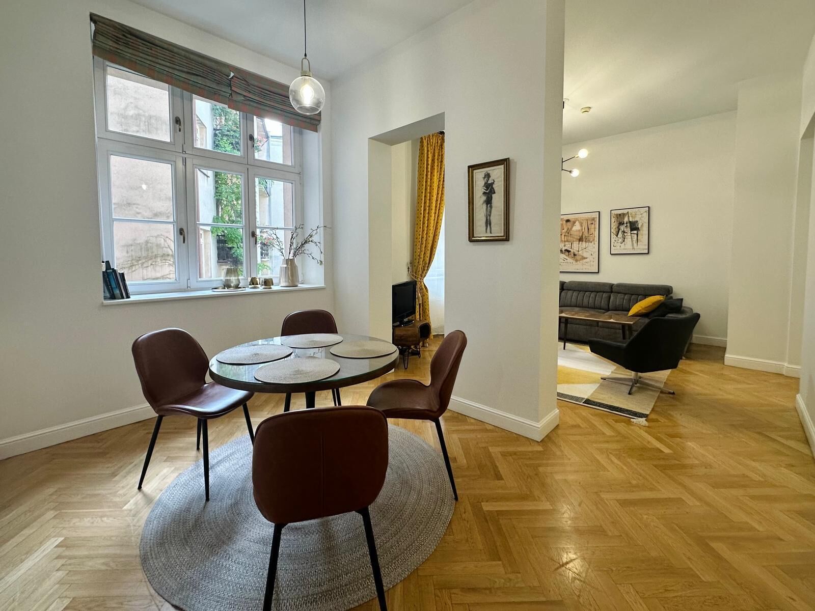 A dining area with a round table, four chairs, a window with curtains, and a view of the outdoors.