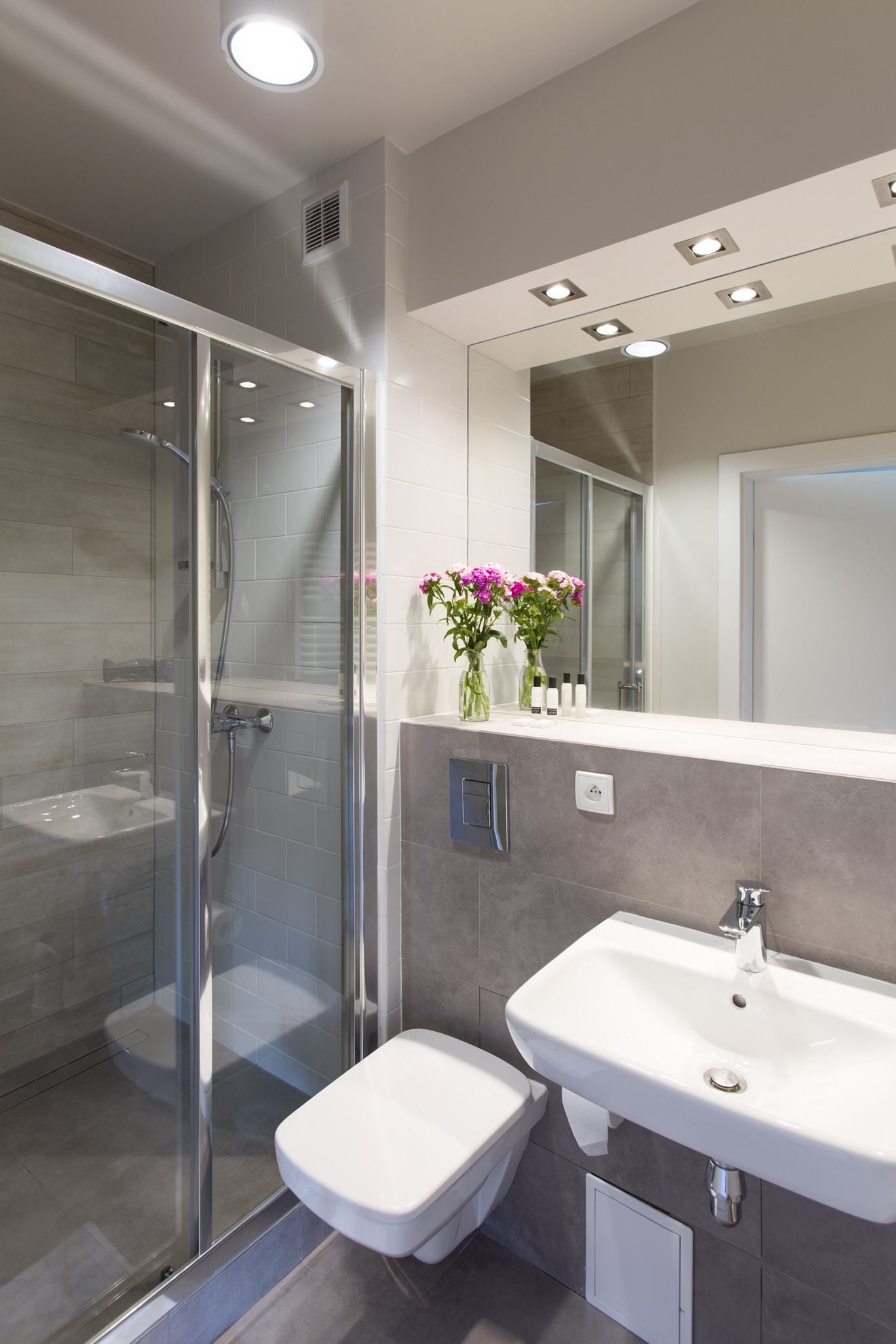Un baño moderno con ducha de vidrio, lavamanos blanco y espejo sobre él.