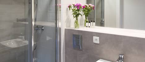 Un baño moderno con ducha de vidrio, lavamanos blanco y espejo sobre él.