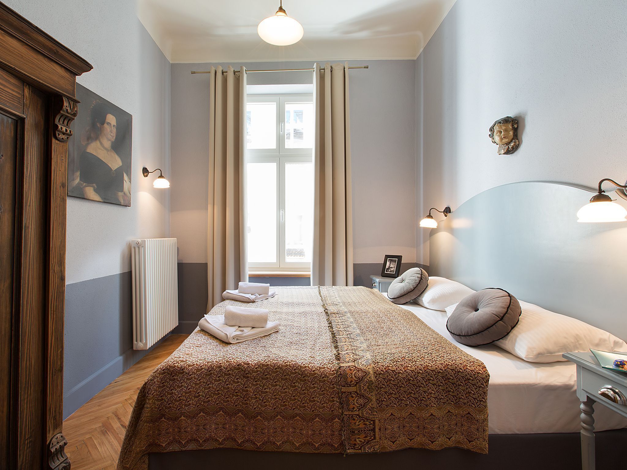 A neatly arranged bedroom with a large bed, a bedside table, a radiator, and a window with curtains.