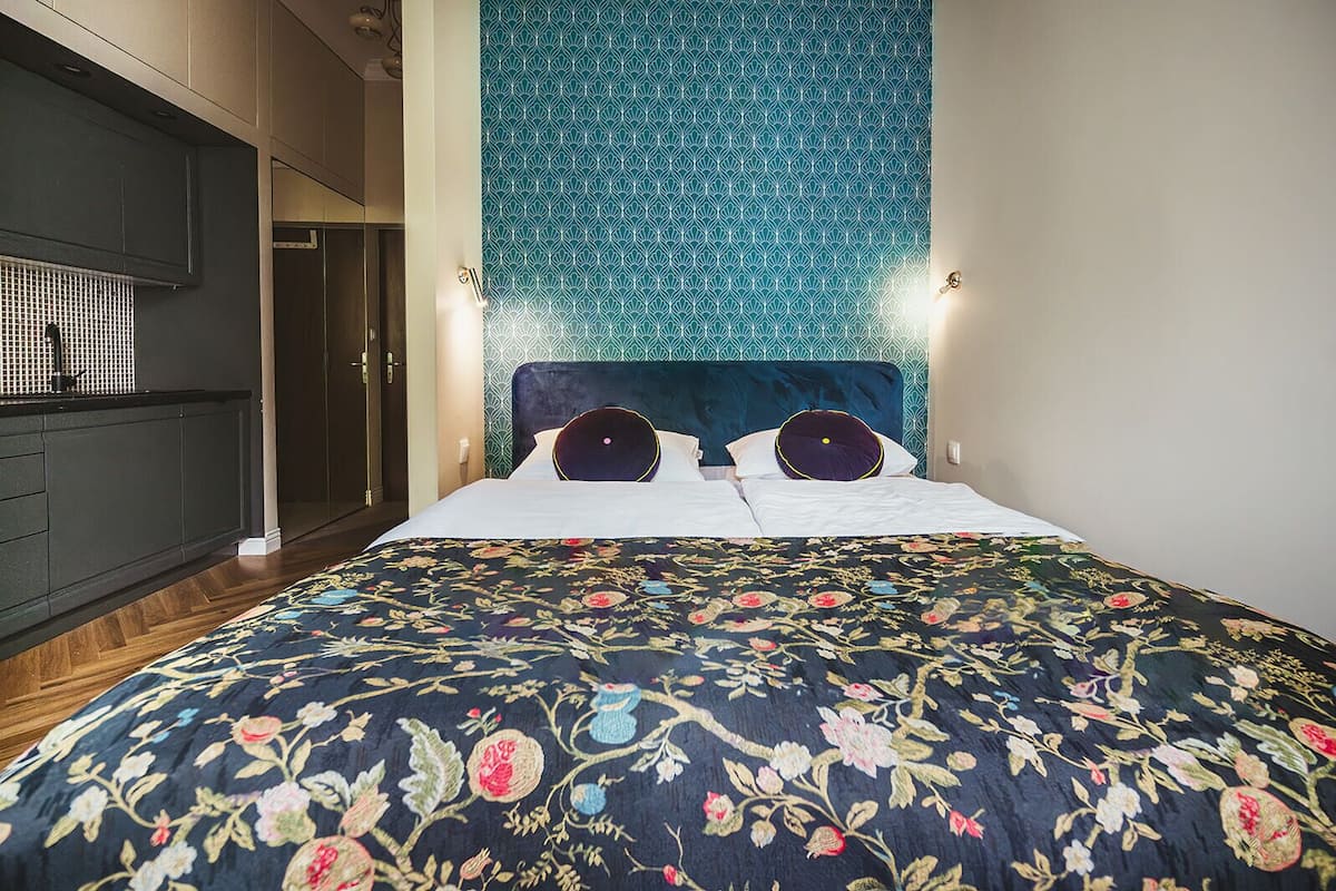 Een slaapkamer met een bed, hoofdeinde, een muur met een geometrisch patroon en een nachtkastje met een lamp.