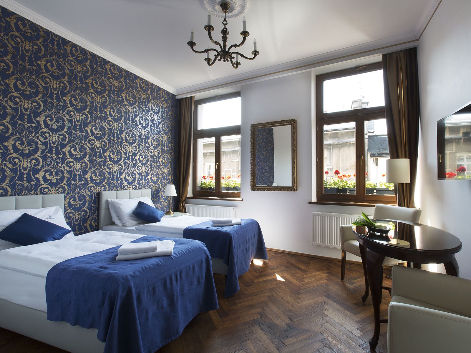 Hotelkamer met twee bedden, een kroonluchter, een raam met uitzicht op de straat en een kleine tafel met stoel.