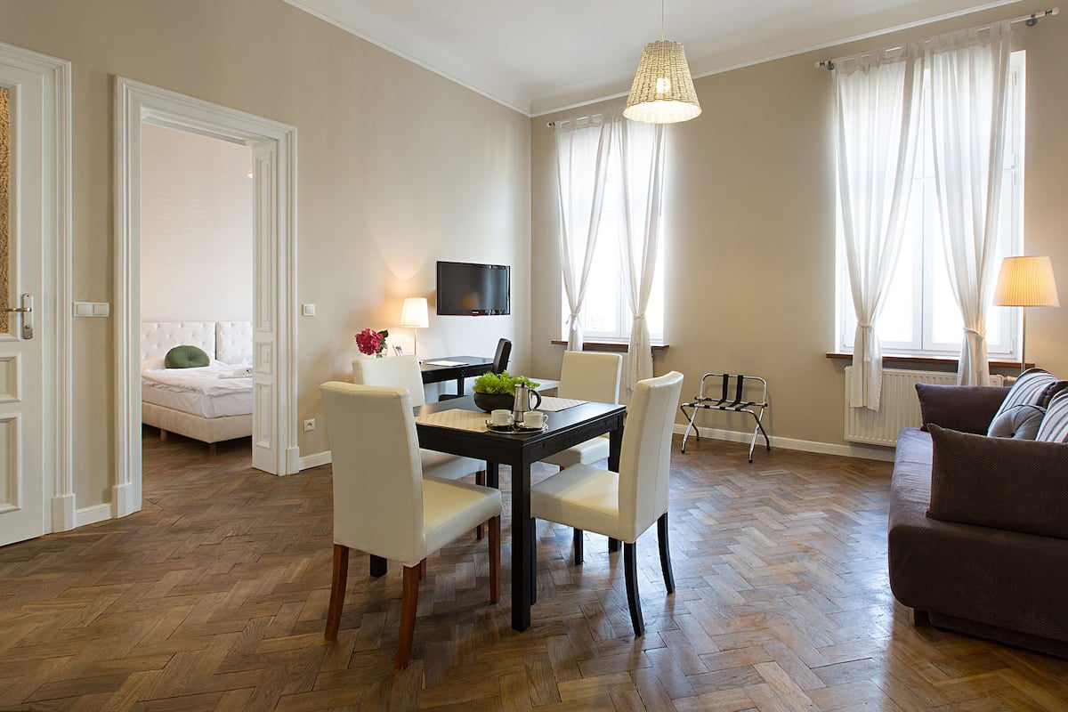 Een moderne woonkamer met een eethoek, een bank, een aan de muur bevestigde televisie en een raam met gordijnen.