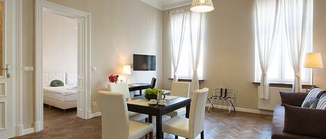 A modern living room with a dining area, a sofa, a TV mounted on the wall, and a window with curtains.