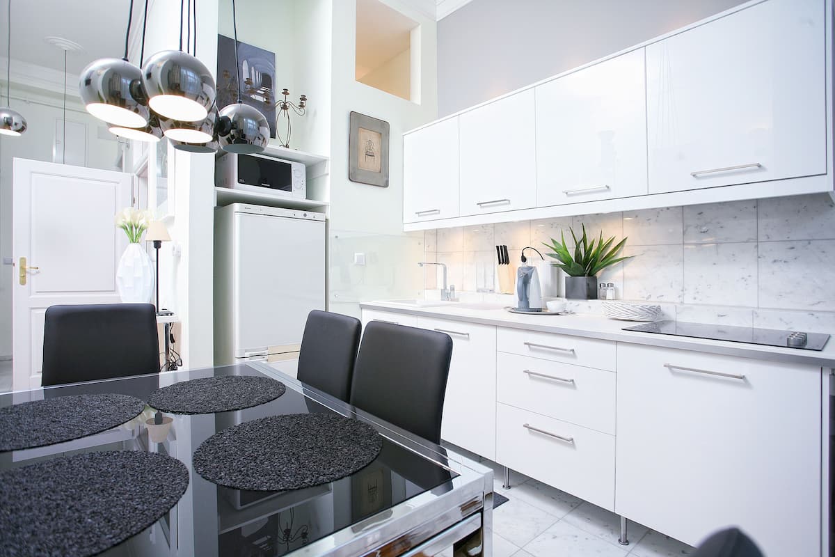 Een moderne keuken met witte kasten, een eettafel met zwarte stoelen en een hanglamp.