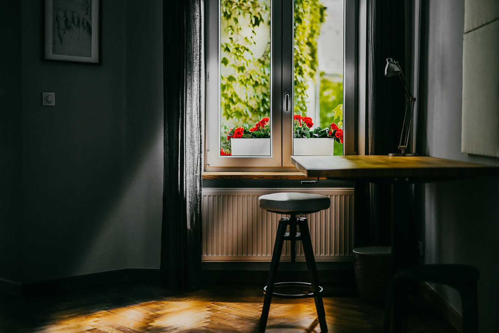 A room with a window, a radiator, a stool, and a desk.