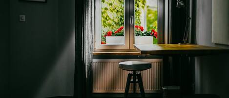 Una habitación con ventana, radiador, taburete y escritorio.