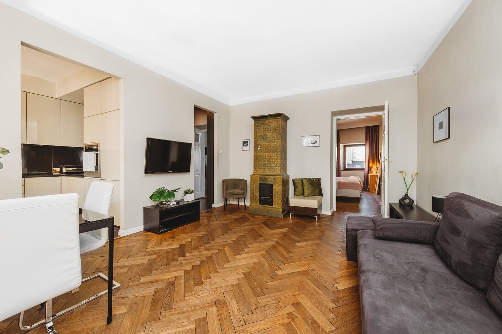 A modern living room with a herringbone wood floor, a fireplace, a sofa, a TV, and a dining area with a table and chairs.