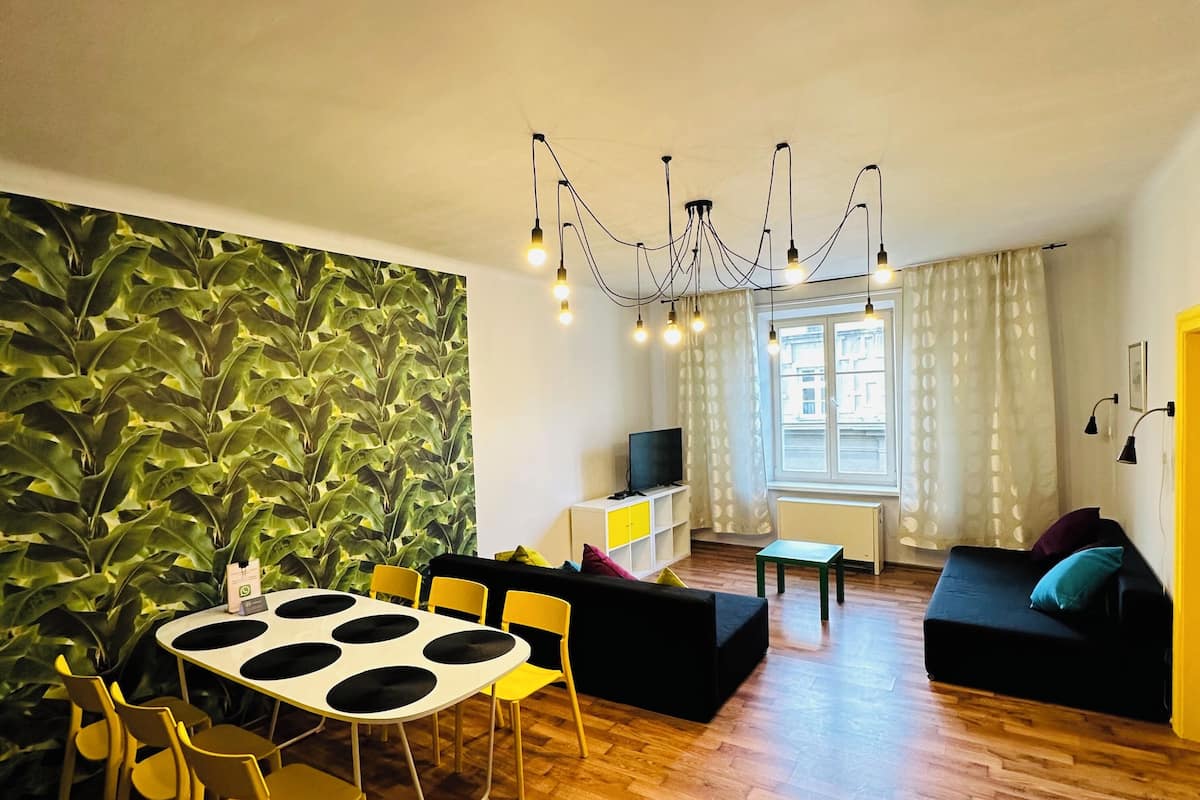 Een moderne woonkamer met een eettafel, gele stoelen, een zwarte bank en een groene salontafel, plus een televisie.