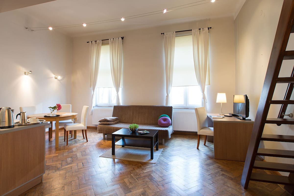 Een moderne woonkamer met een bank, salontafel en een eethoek met een tafel en stoelen. Er is een televisie en een lamp op een bijzettafeltje.