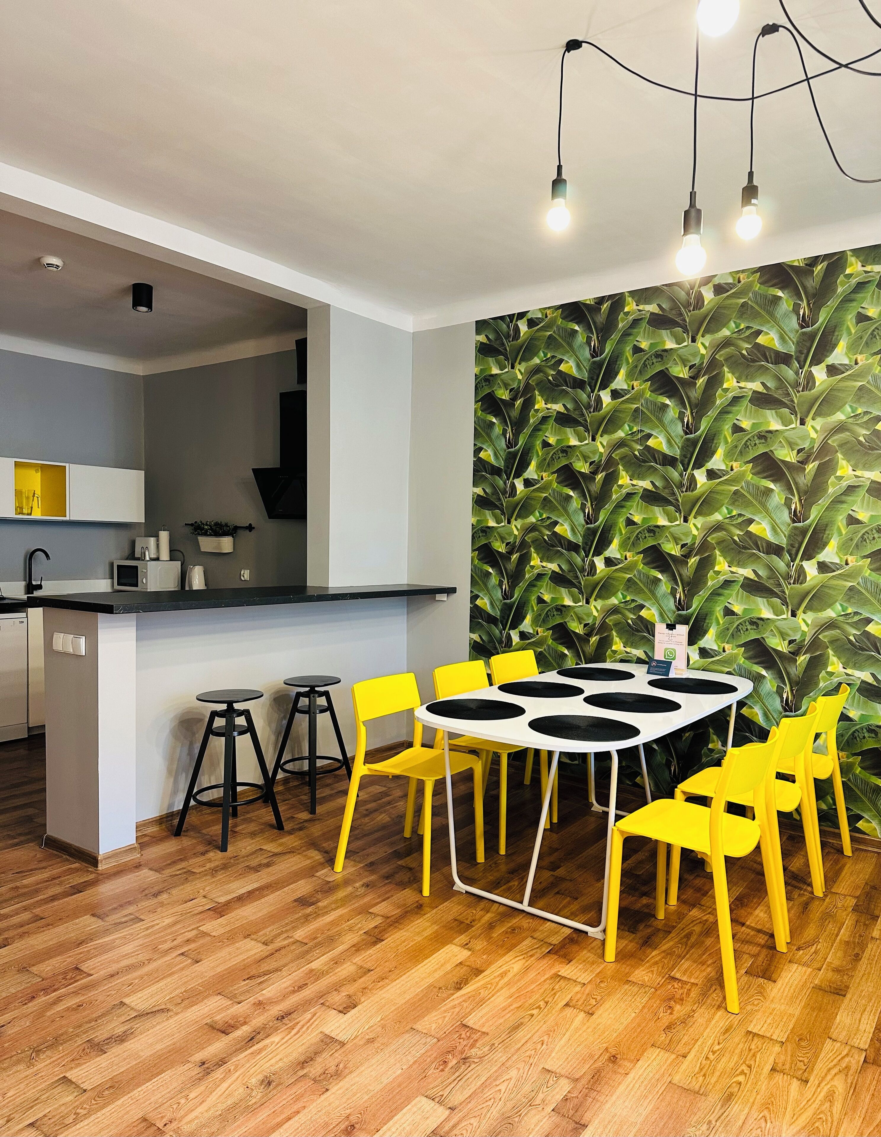 A modern kitchen with a white countertop, black stools, and a yellow dining table with black circular centerpieces.