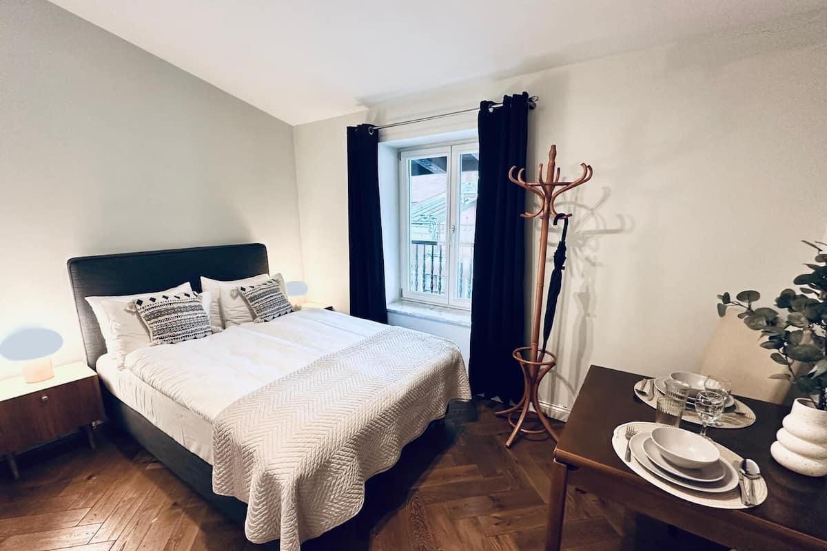 Een netjes ingerichte hotelkamer met een bed, een eettafel, een kapstok en een raam met gordijnen.