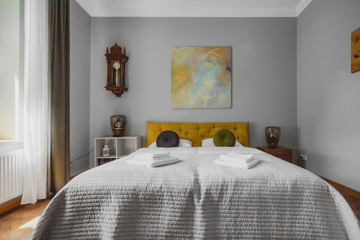 Een keurig opgemaakt slaapkamer met een groot bed, een wandklok, een schilderij en een nachtkastje met een lamp.