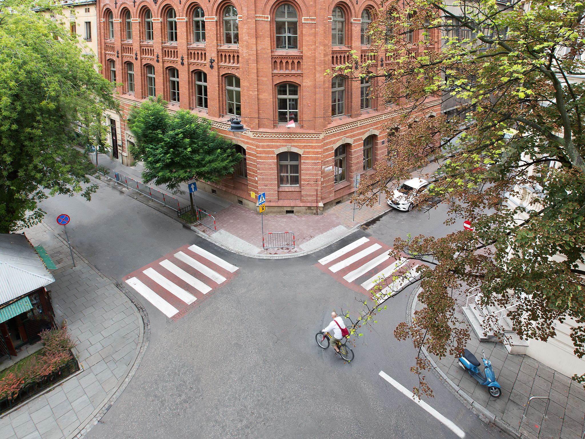 A street intersection with a pedestrian crossing, a cyclist, and a parked scooter.