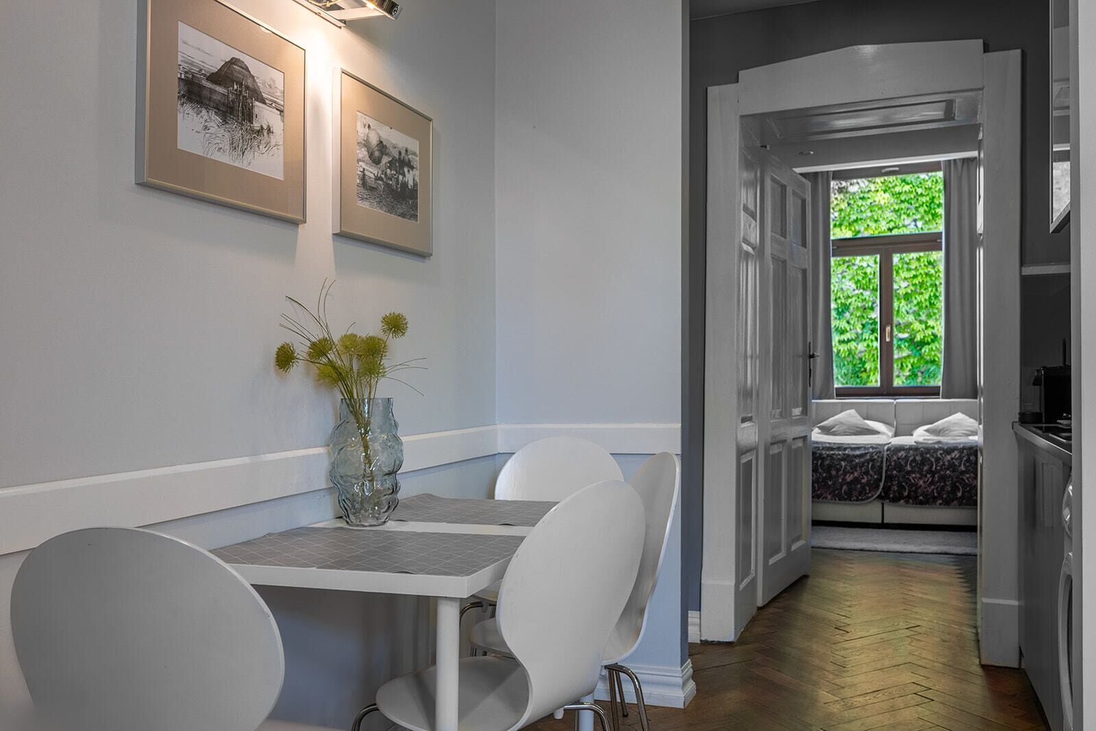 Een eethoek met een tafel, stoelen, een vaas met bloemen en ingelijste foto's aan de muur.