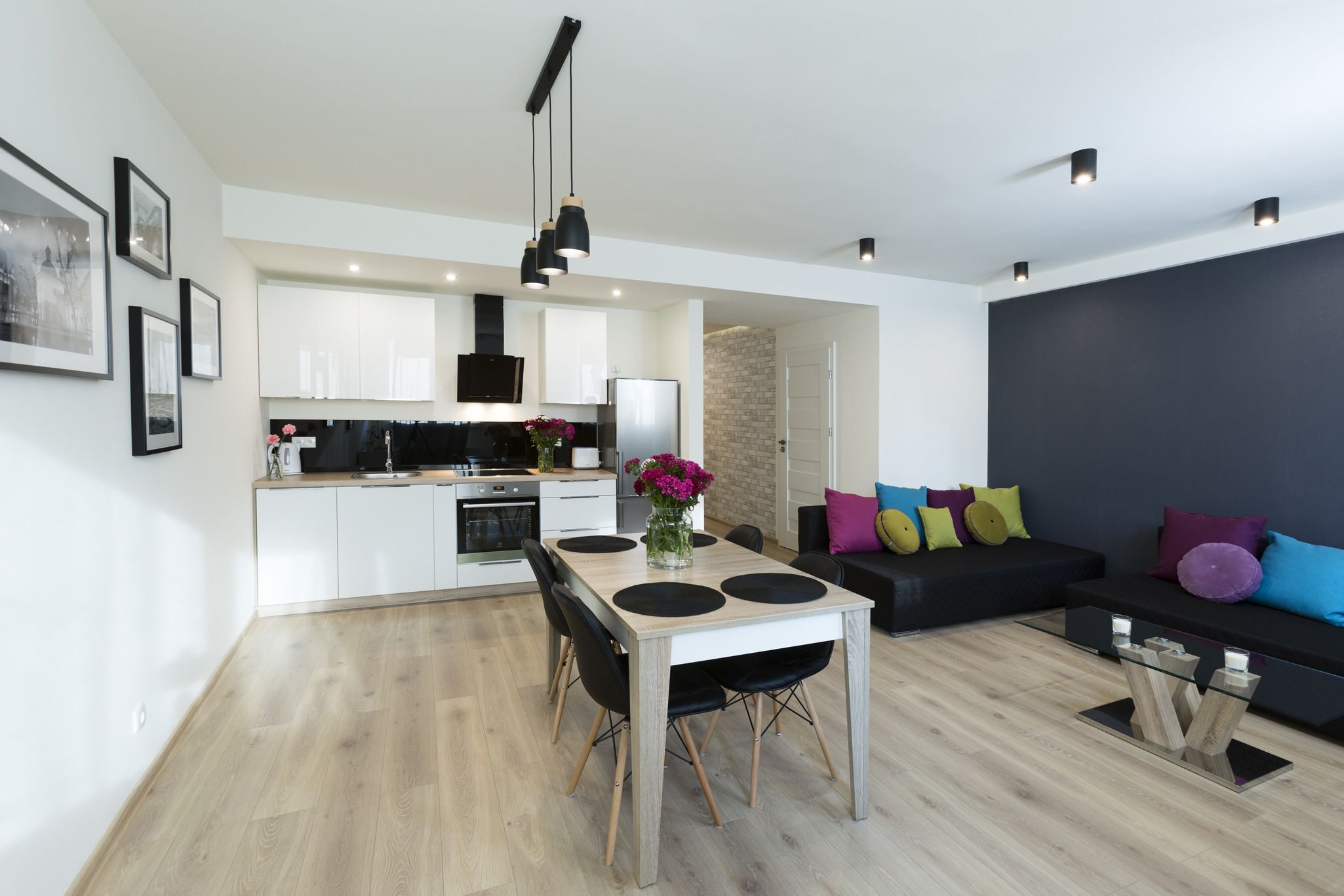 Una cocina moderna con armarios blancos, encimera negra y un comedor con mesa y sillas de madera.