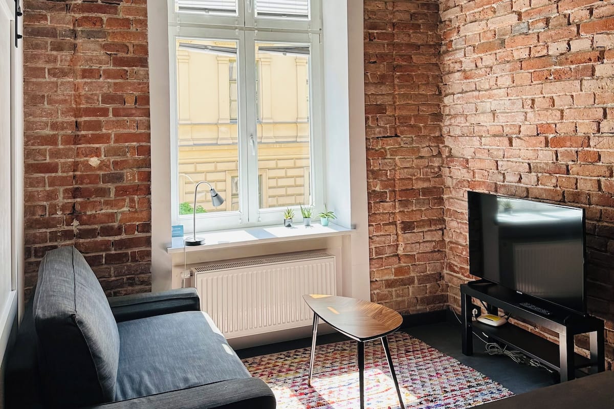 Een gezellige woonkamer met een bakstenen muur, een groot raam, een bank, een televisie en een hanglamp.