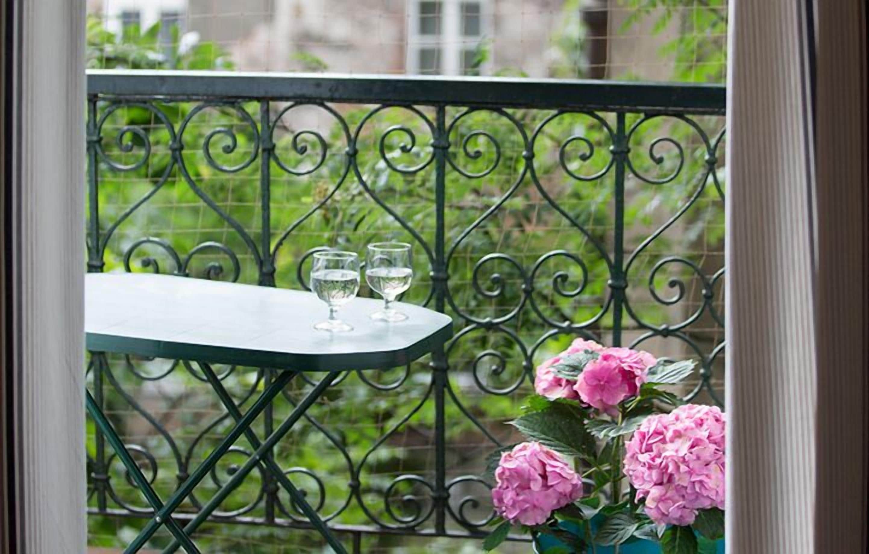 Een balkon met een smeedijzeren hekwerk, een tafeltje en twee glaasjes water.