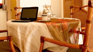 A dining area with a laptop on a table, surrounded by wicker chairs.